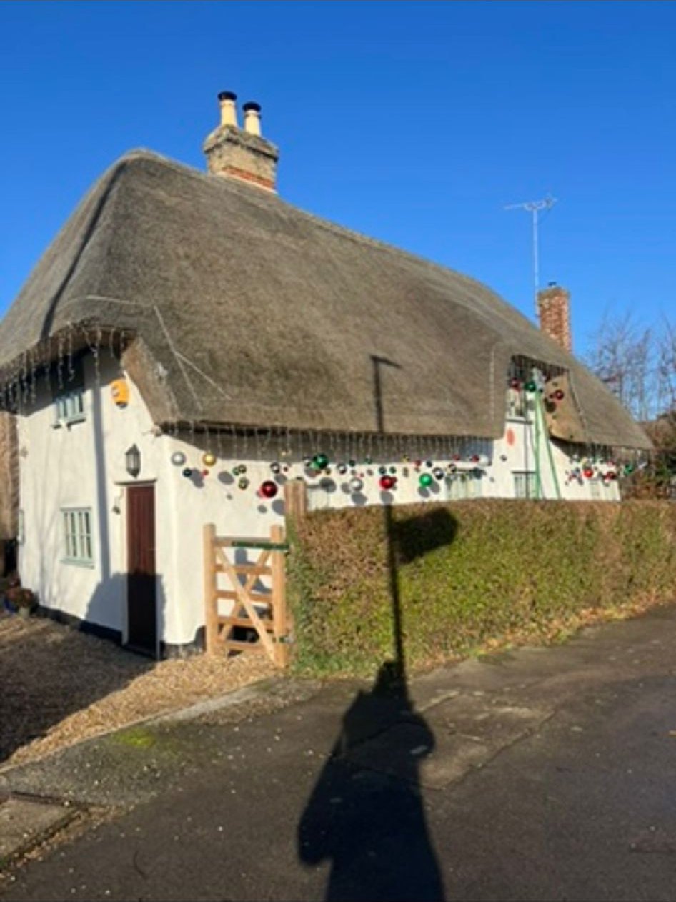 A whitewashed thatched cottage on a village lane in the Abingtons under a clear blue sky